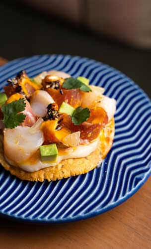 Tostada de Vieiras e Pesca do Dia, leche de tigre de coral de vieiras, salsa macha de ají panca e cancha chulpi, purê de sarandajas e coentro - Mares de La Peruana