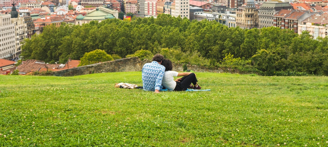 Couple watching a beautiful panoramic view of Bilbao sitting in the park on the hill above the Old Town