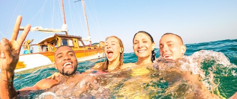 Giovani che nuotano vicino a una barca a vela a Ibiza Giovani che nuotano vicino a una barca a vela a Ibiza