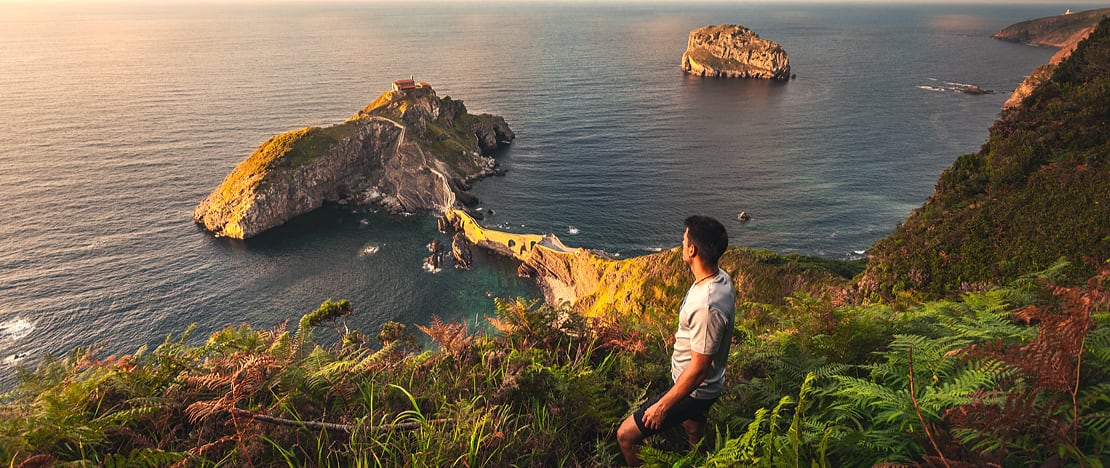 Ein Tourist betrachtet die Kapelle San Juan de Gaztelugatxe in Bizkaia, Baskenland Ein Tourist betrachtet die Kapelle San Juan de Gaztelugatxe in Bizkaia, Baskenland